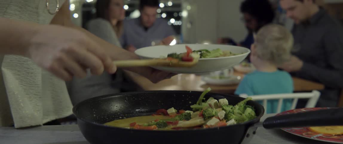 Vegetables being spooned from sizzling pan onto plate with fresh culinary motion