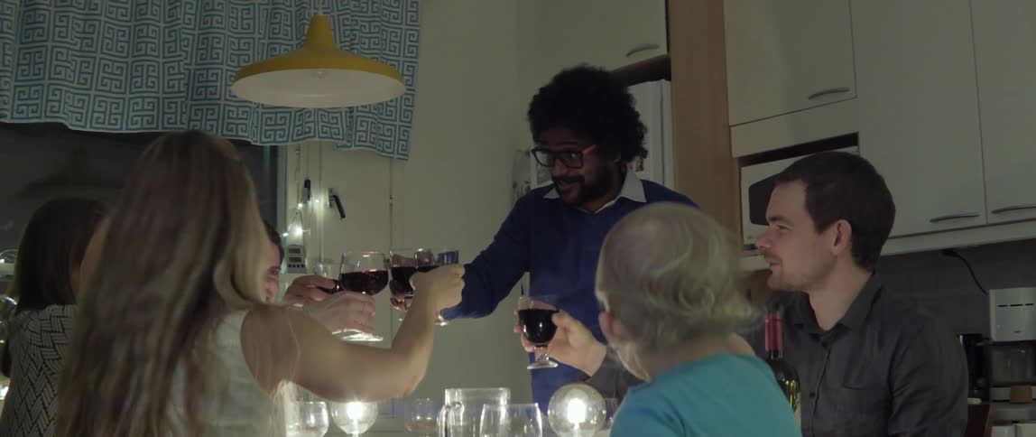 People talk and drink at a dinner table before one man makes a toast