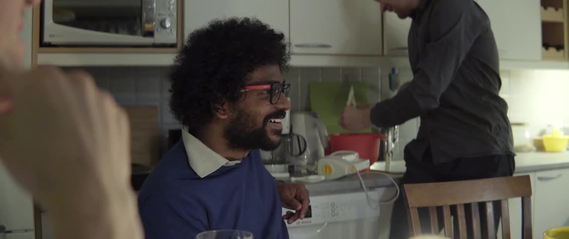 Candid moment of a man laughing while talking with friends at a dinner table.