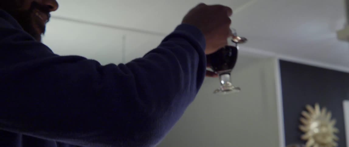 A man rises from his seat at a dinner table and taps his glass to start a toast