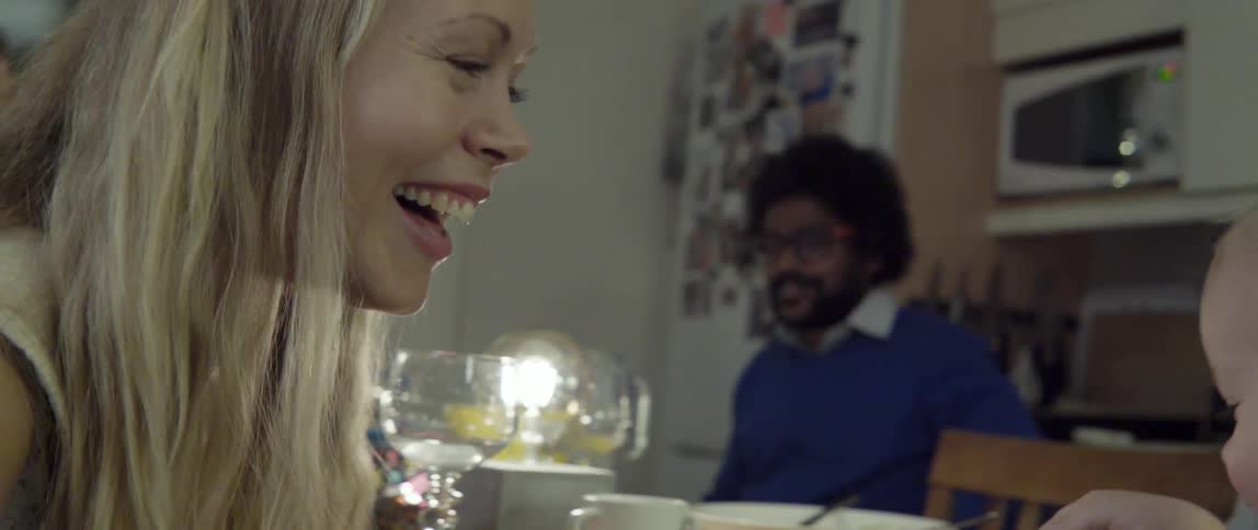 A woman laughs while a baby tears a piece of bread