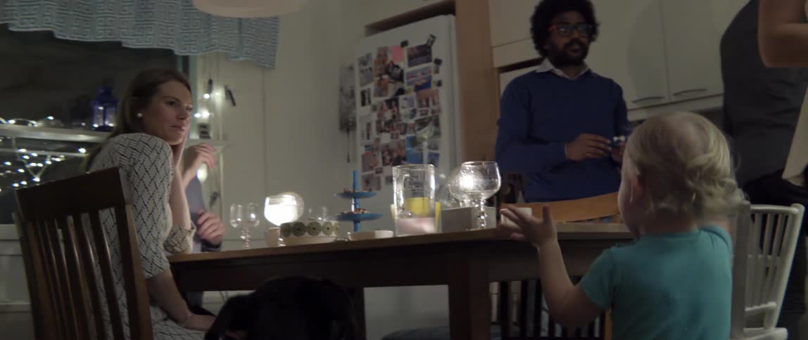 A group of people, a baby and a dog interacting around a dining table at night