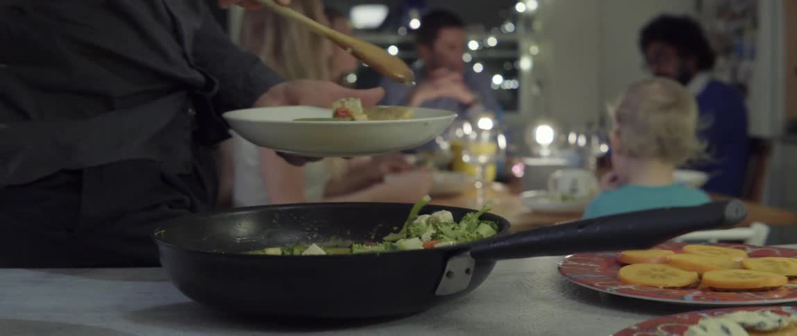 Man spooning sautéed vegetables from pan onto plate with fresh kitchen motion