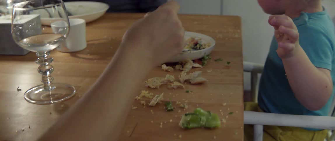 A child has thrown food all around the table as he laughs