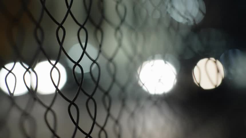 Cars are driving outdoors at night near a fence
