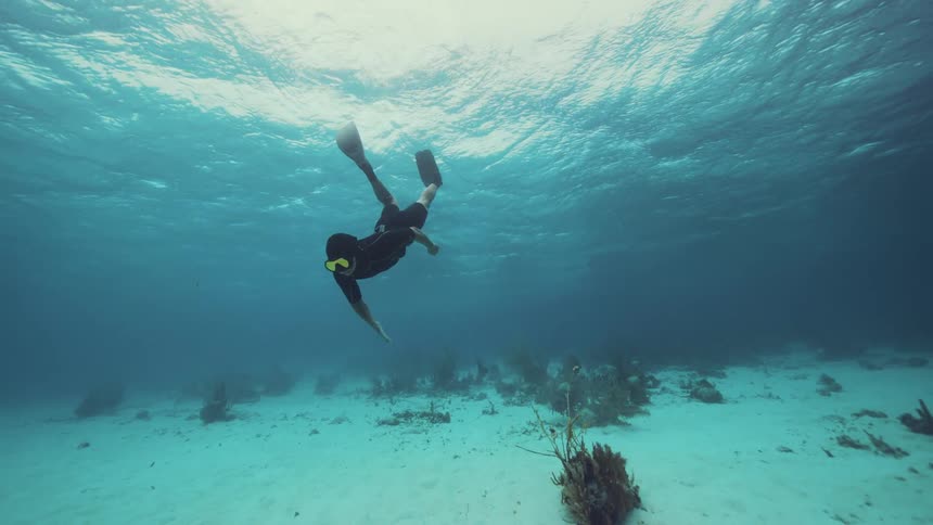 Man wearing goggles and flippers swims underwater just above seafloor