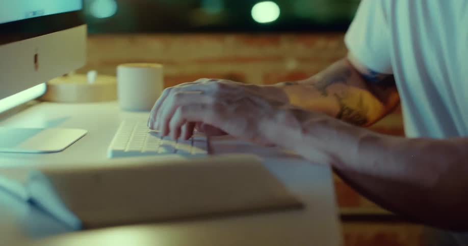 A man sitting at a desk near a window typing on a wireless keyboard