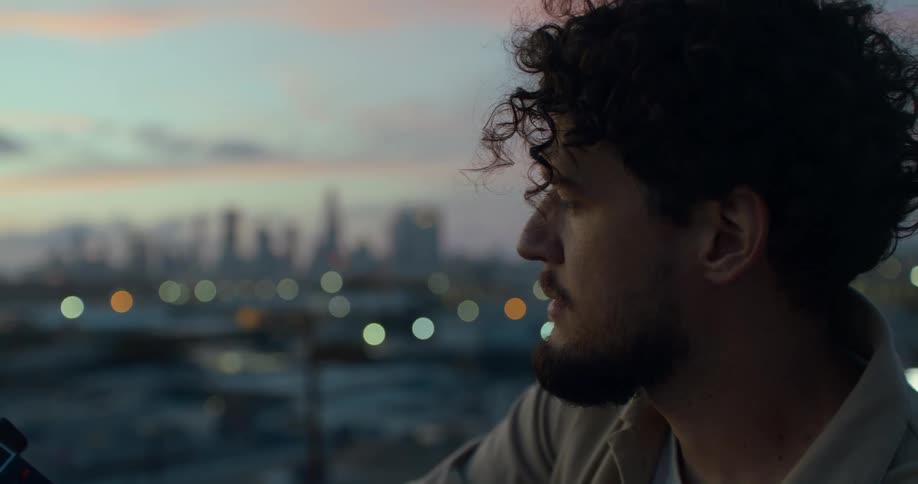 Man with beard and curly hair looks into space with city skyline in the background