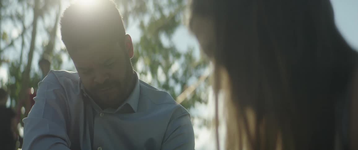 Father frowns and smiles while watching daughter play outdoors on a sunny day
