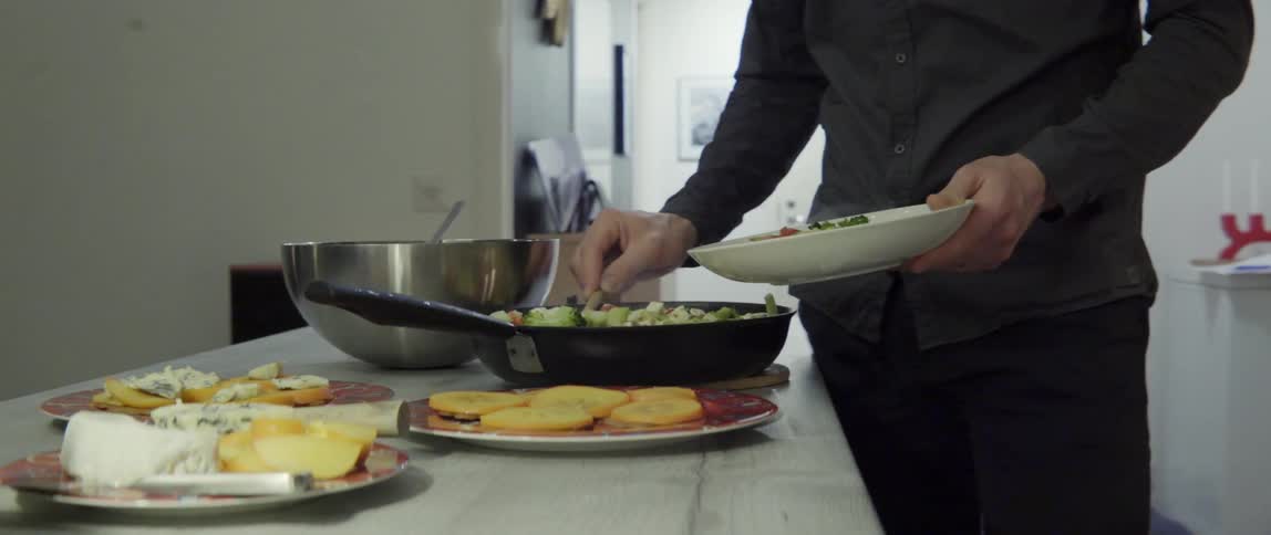 Man serving hot food from steaming skillet onto plate with focused care