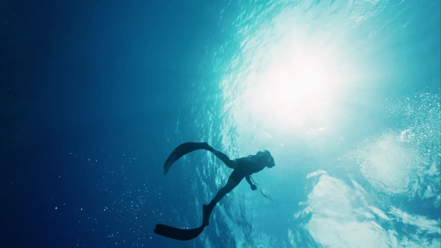 A person is swimming towards the surface of the water