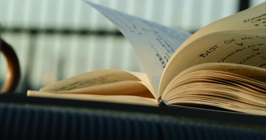 A coffee cup sits beside a book on a table as the pages turn