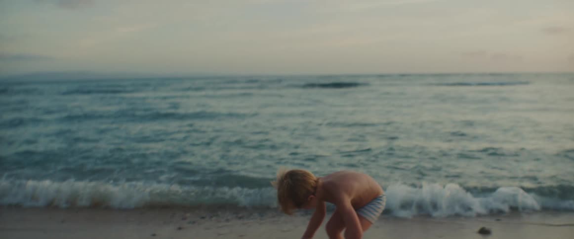 A little boy is playing on a beach throwing rocks into the water as waves roll into shore