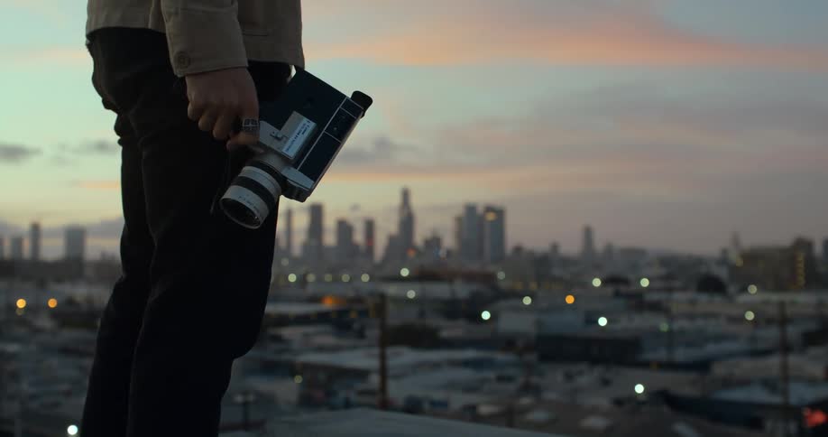 Person stands overlooking city with film camera