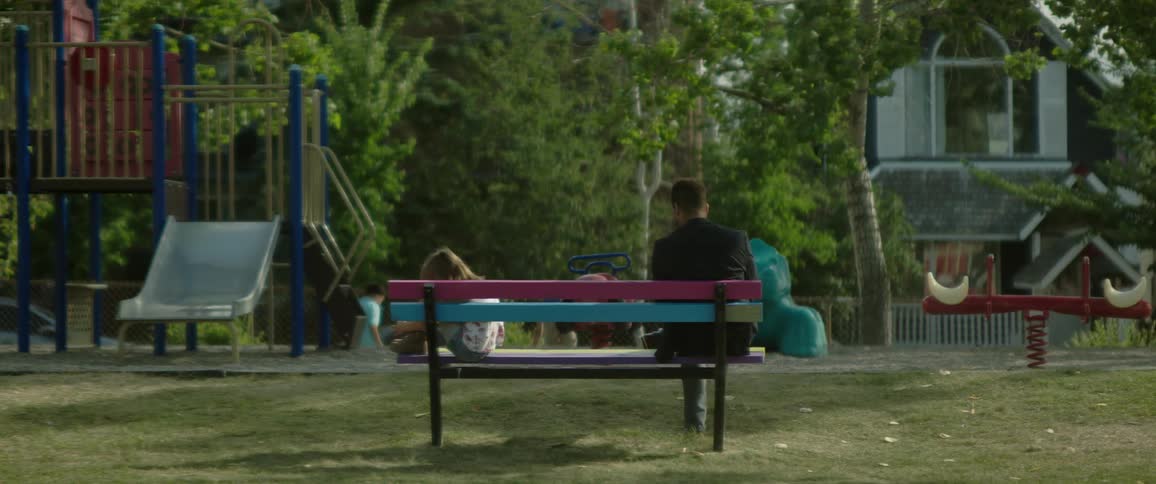 A man is sitting on a park bench and a little girl is sitting at the other end of the bench holding her knees