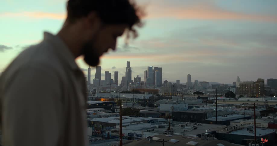 A man is standing in a downtown city as the sun is setting