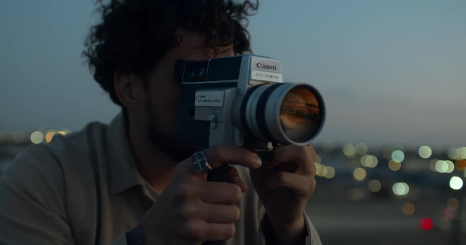 A man raises a video camera up to his face as he looks over a city