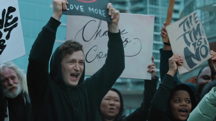 People holding banners protest in the street with high rise buildings in the background