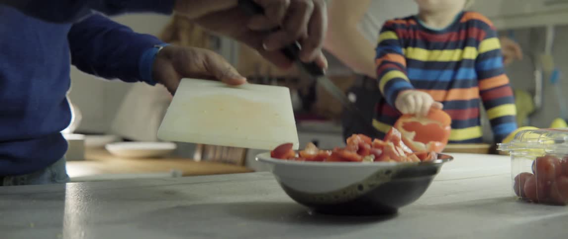 A man is cutting peppers and putting them in a bowl as a child watches