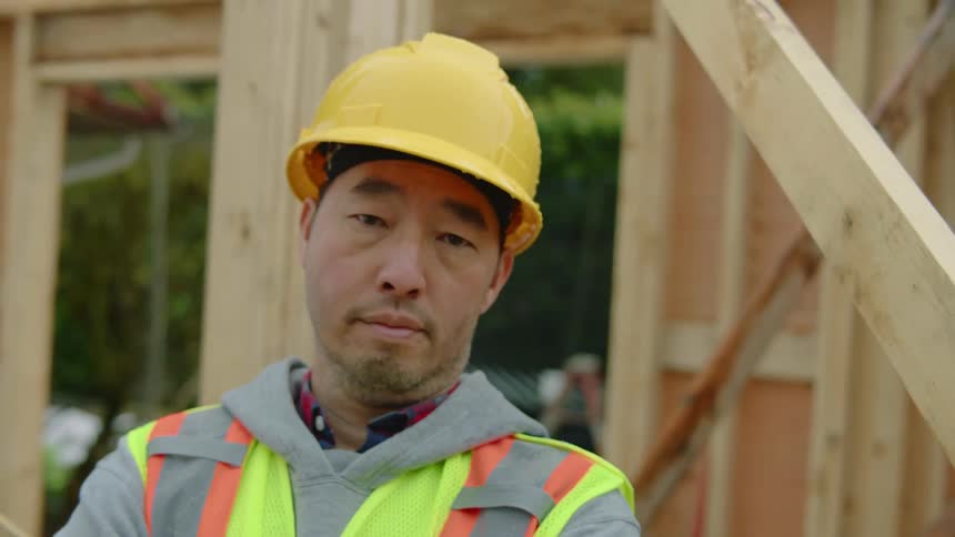 A male construction worker wearing a yellow hardhat is standing still