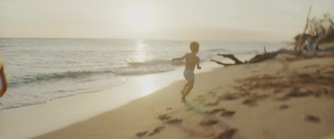 A little boy runs down the beach as he is chased by his mother and brother
