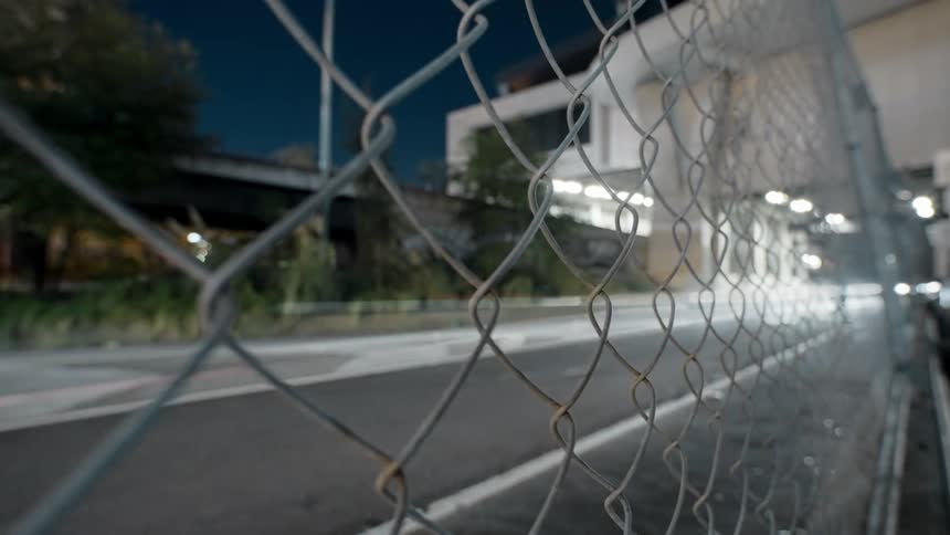 A chain link fence beside a busy road at night