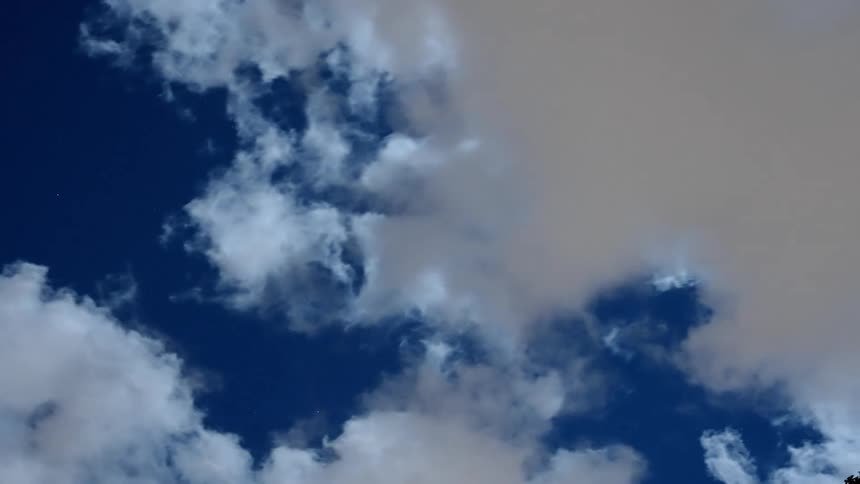 Cumulus clouds move across a deep blue sky