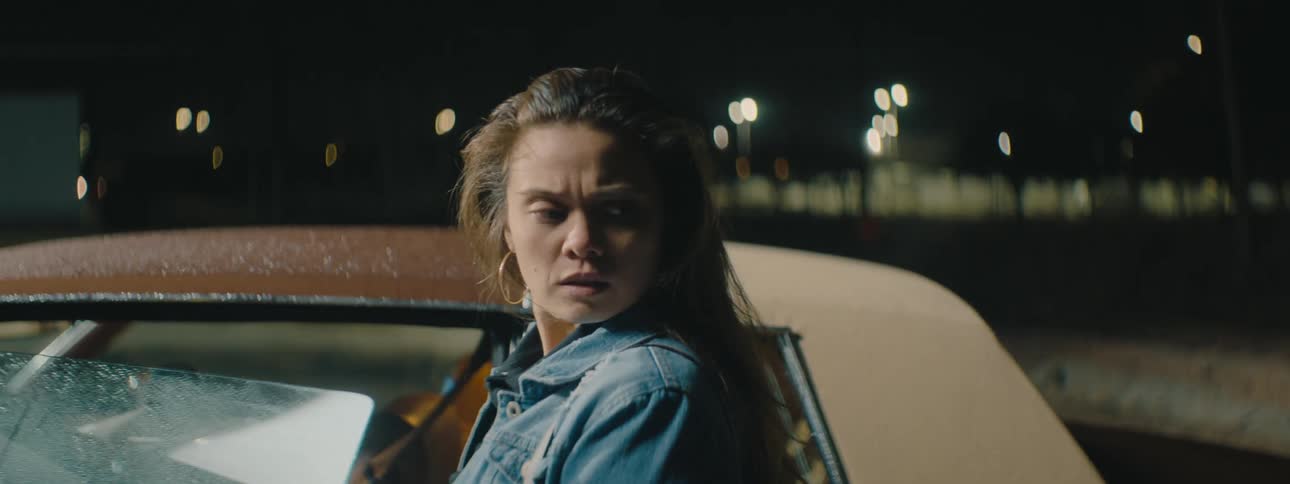 A woman about to get in to her car at night nervously looks behind her