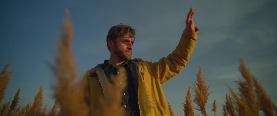 A man is walking through a grassland area at dusk
