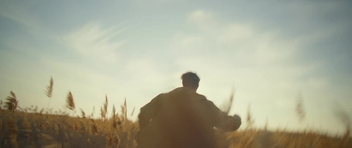 Man with yellow raincoat runs across the field at sunset
