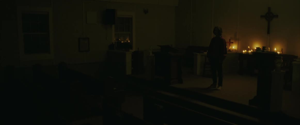 A person stands in a dark church lit up only with candles