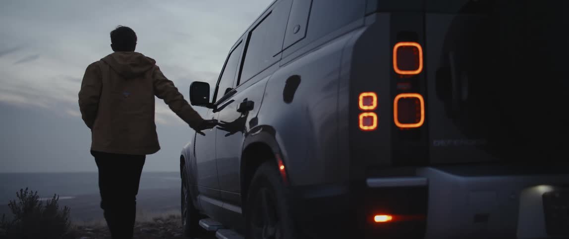 A man gets out of a truck that is parked on a cliff in front of a large waterway