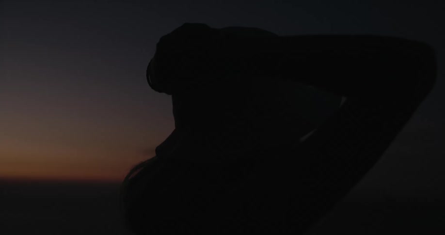 Woman putting her hands on her hat is silhouetted against the red sky at dusk