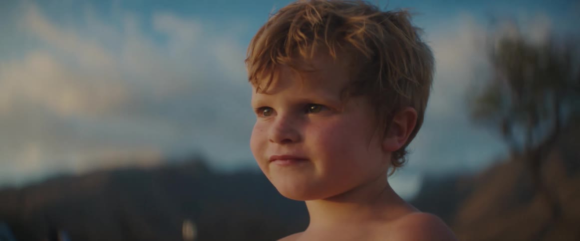 A boy smiles as he stands with mountains in the background