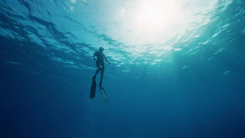 A scuba diver is swimming underwater as the sun shines brightly through the water