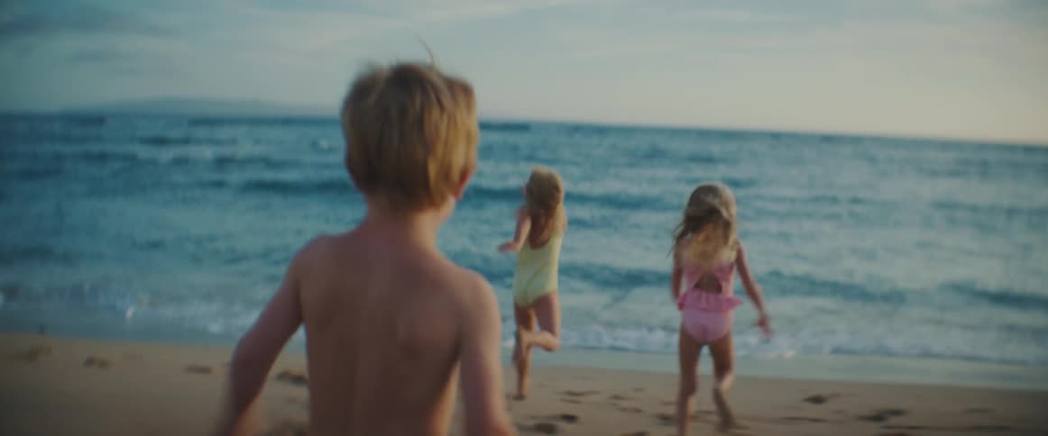 Three siblings race toward the ocean at sunset during a joyful, carefree beach moment