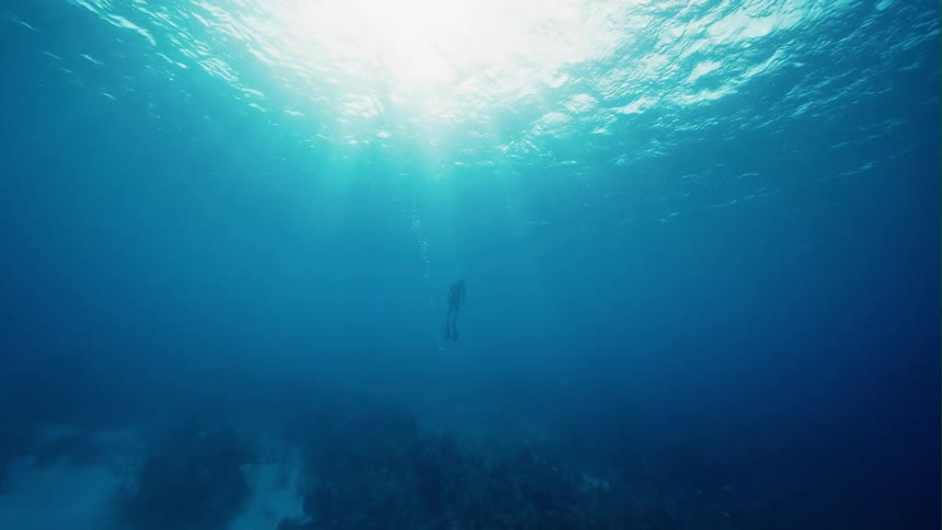 Silhouette of a person scuba diving in clear water as the sun shines above