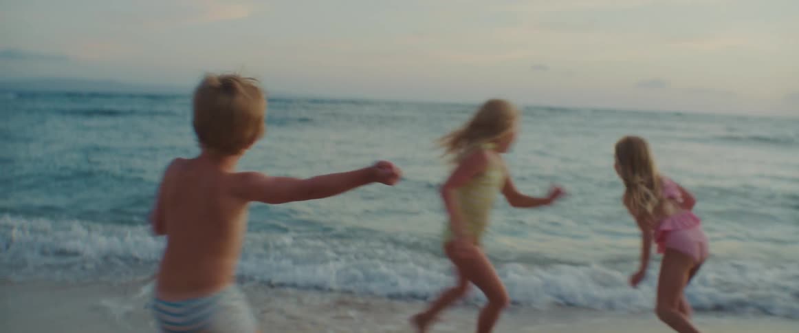 Three kids run on the beach together and play