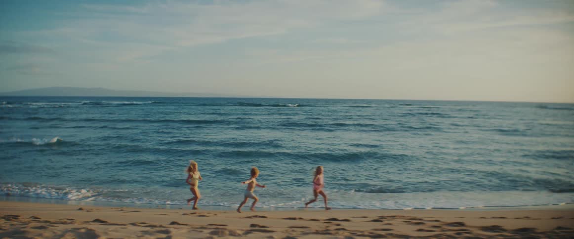Young children are running and playing on a beach as the waves roll into shore