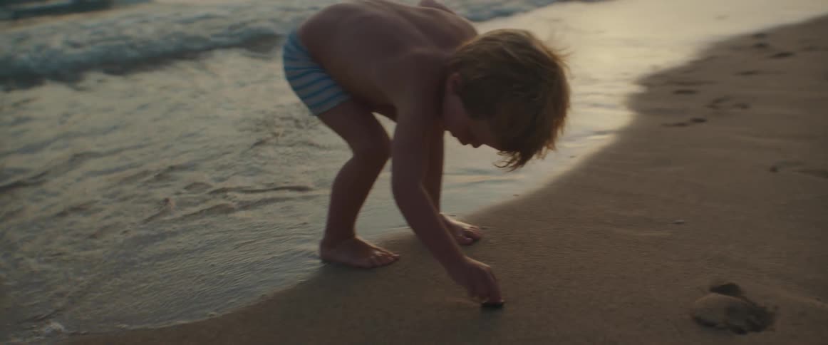 A little boy is playing on a beach throwing rocks into the water as the waves roll into shore
