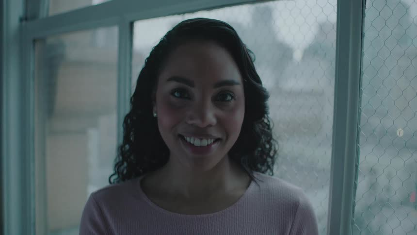 Woman with curly hair and pink sweatshirt faces the camera with eye contact and smiling
