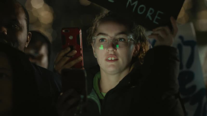 A group of people hold signs up and take pictures with their cell phones as they stand outside in the dark