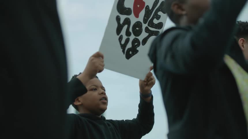 A boy in a group of protestors holds up his sign and chants with the crowd
