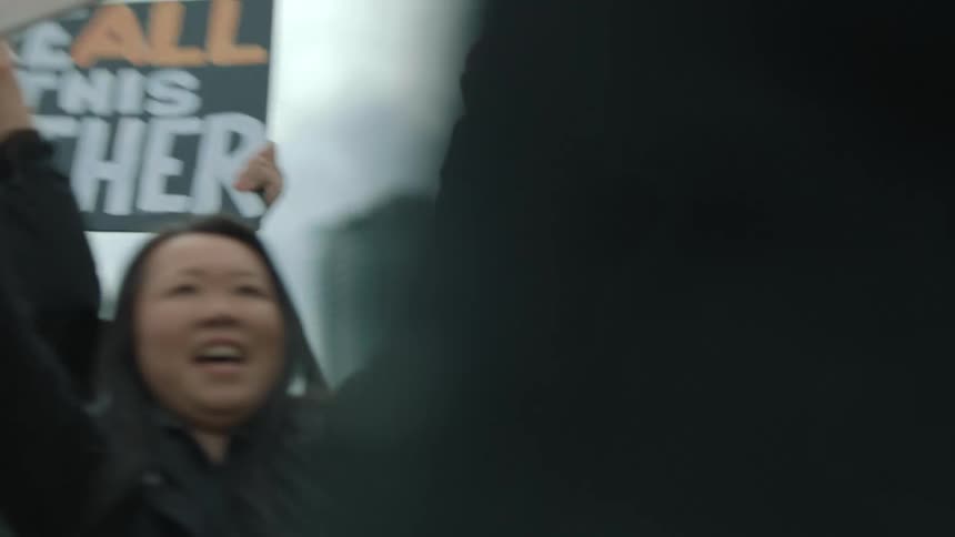 A diverse group of protestors hold up signs with positive sayings cheering and clapping