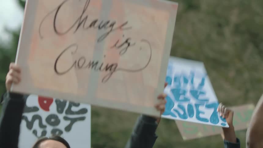 A group of diverse and united protestors hold up signs and cheer