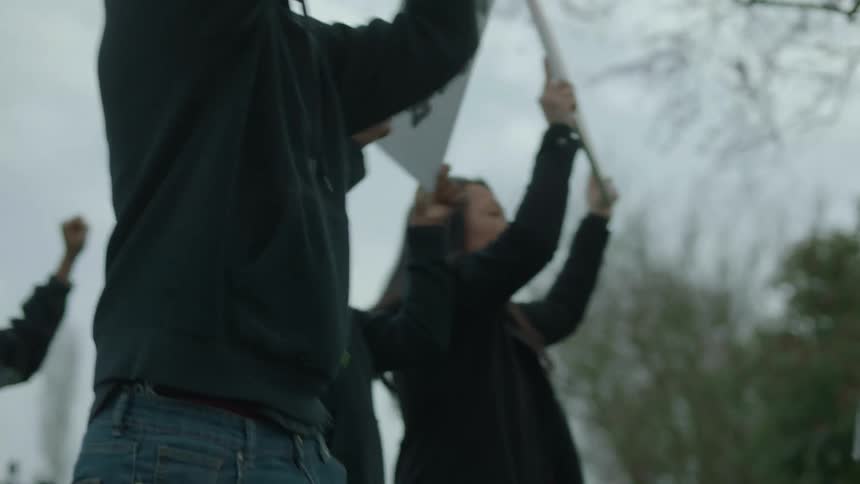 A diverse group of protestors marching and holding up signs on a gray cloudy day