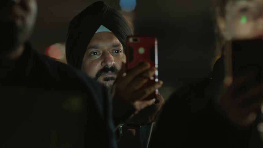 People stand outdoors listening and smiling as they take video with smartphones
