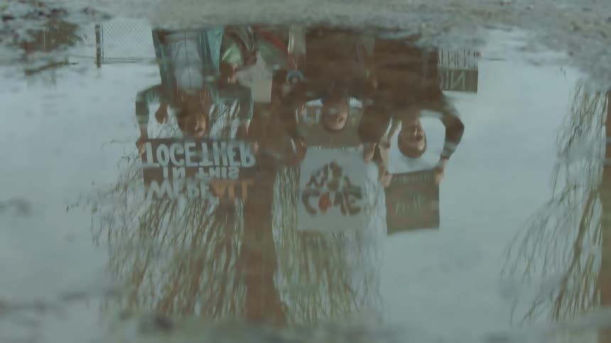 The reflection of a group of people marching in a protest shows in a puddle on the ground