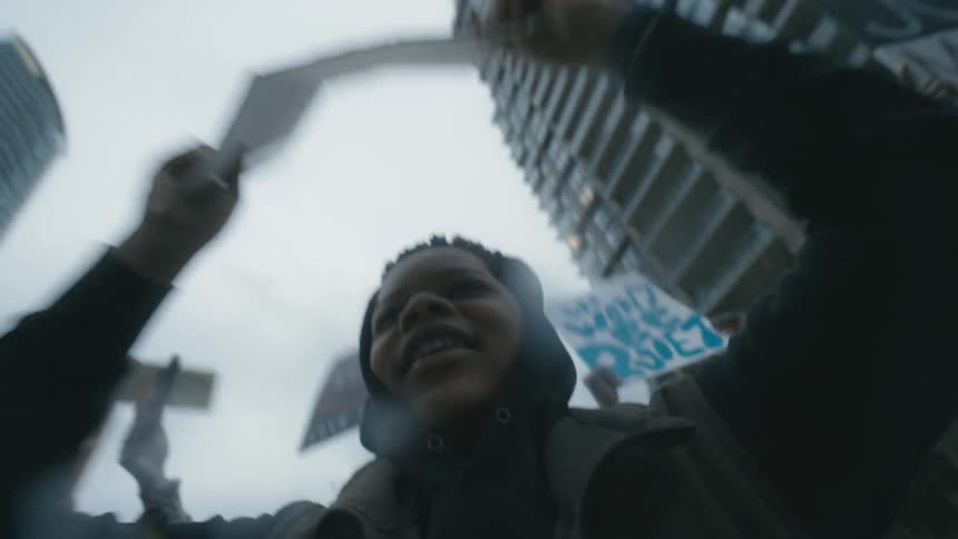 A young boy yells and holds a sign up as a woman behind him films the rally with her cell phone