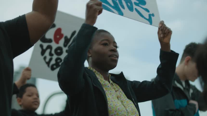 A woman holds a sign above her head while marching with a group of protesters